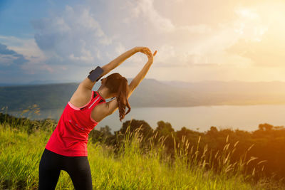 Rear view of young woman exercising on mountain against cloudy sky during sunset