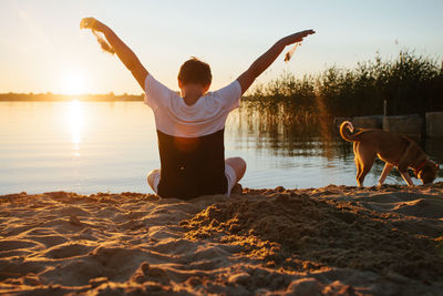 Rear view of woman with dog in water at sunset