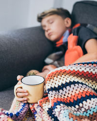 Sick boy sleeping with woolen blanket, hot water bottle and mug. sad teen with the flu rests at home