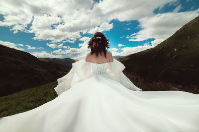 The bride turns her back and runs away in a white dress with flowing hair in a green valley against