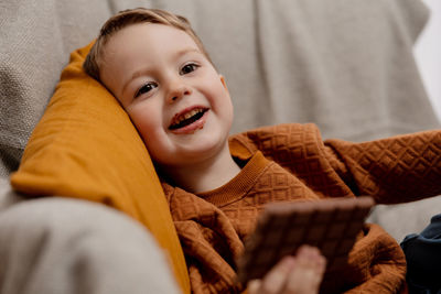 Little adorable boy sitting on the couch at home and eating chocolate bar. child and sweets