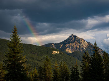 Scenic view of mountain landscape at dusk with rainbow and dark clouds