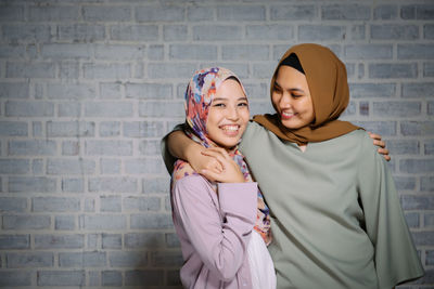 Portrait of smiling woman with friend standing against brick wall