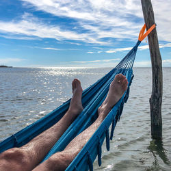 Low section of man relaxing in hammock over sea against sky