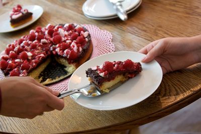 Cropped hands of people with strawberry cake on table