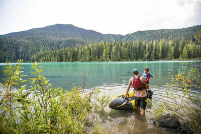 Father carries son through water into inflatable boat, father son trip