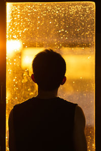 Rear view of man looking through window at night