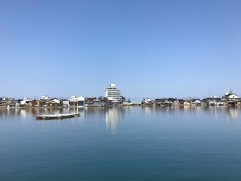 Buildings by sea against clear blue sky