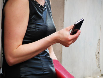 Midsection of woman using mobile phone while standing by wall