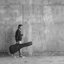 Full side view of a man carrying a guitar on the wall