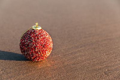 Close-up of red christmas ball on sandy beach at sunset