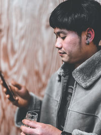 Young man using mobile phone while holding drinking glass