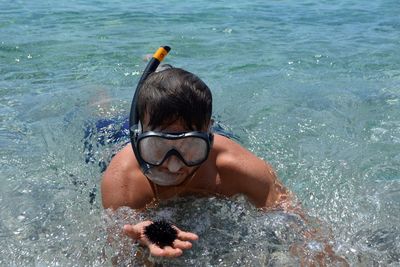 High angle view of man holding sea urchin while snorkeling in sea