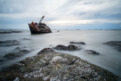 Abandoned boat in sea against sky