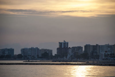 Sea by city against sky during sunset