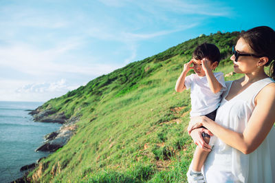 Side view of woman photographing while standing against sea against sky