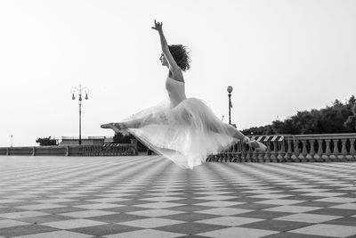 Ballet dancer jumping on tiled floor against clear sky