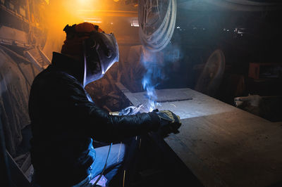 Village workshop, welding in an old garage. an unrecognizable man repairs a metal part wearing