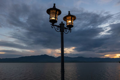 Street light by lake against sky during sunset