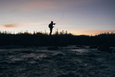 Silhouette of man fishing against sky during sunset