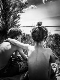 Rear view of shirtless boy and woman against sky