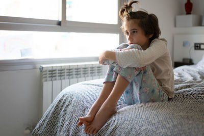 Full length of woman sitting on bed at home