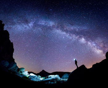 Low angle of tourist with headlamp standing on cliff and admiring amazing starry sky at night in pyrenees