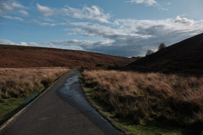 Road amidst field against sky