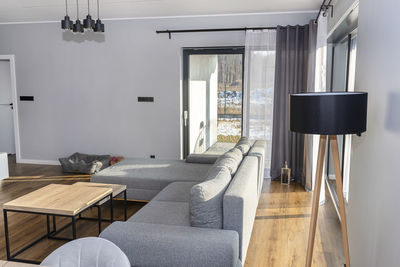 A modern and simple living room in the house with a gray sofa, large patio windows and tables.