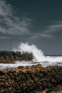 Waves splashing on rocks at shore against sky