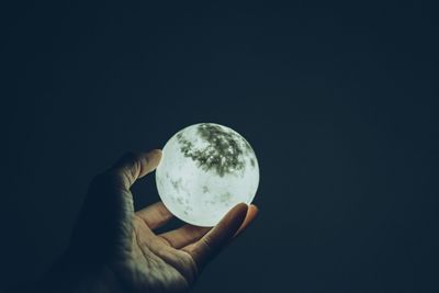 Close-up of hand holding crystal ball against black background