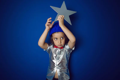 Christmas boy child holding a star in a silver shirt blue hat and red bow tie stands in the studio