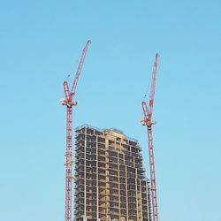 Low angle view of cranes at under construction site against clear blue sky