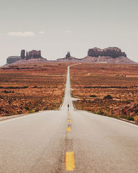 Man walking on road leading towards mountain against sky