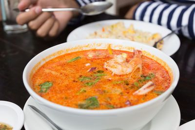 Cropped hand of person holding soup in bowl on table