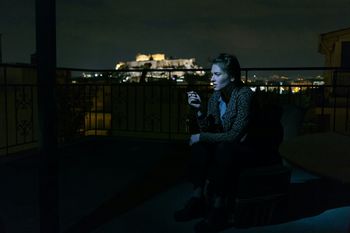 WOMAN SITTING ON ILLUMINATED BUILDING AGAINST SKY