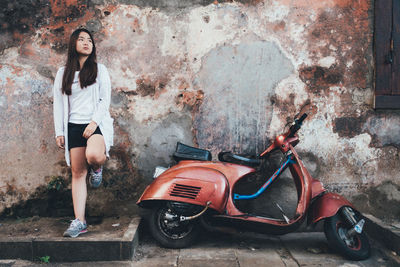 Young woman standing by motor scooter against wall