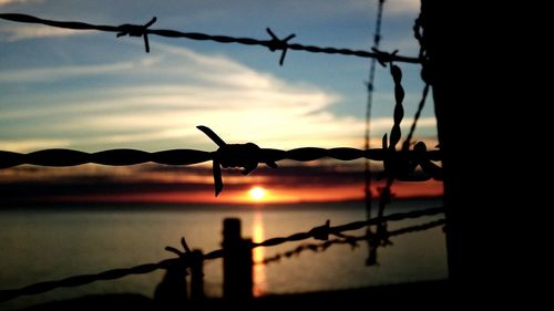 Silhouette of barbed wire against sky during sunset