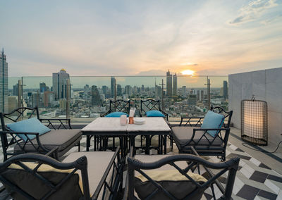 Empty chairs and tables in city against sky during sunset