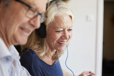 Smiling senior woman wearing headphones by man at home