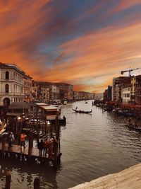 Boats in canal by buildings in city against sky during sunset