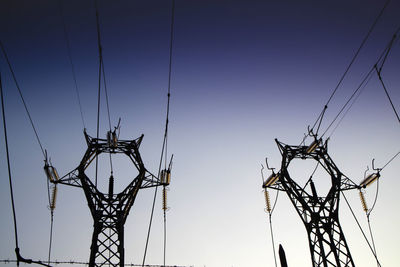 Low angle view of silhouette electricity pylons against clear sky