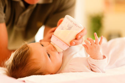 Midsection of father feeding daughter milk with baby bottle on bed