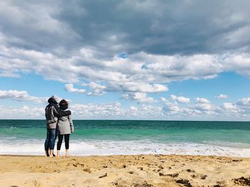 Rear view of friends on beach against sky