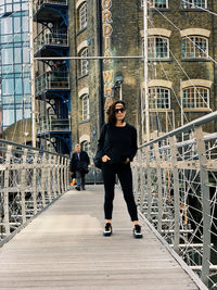 Portrait of woman wearing sunglasses standing on footbridge in city