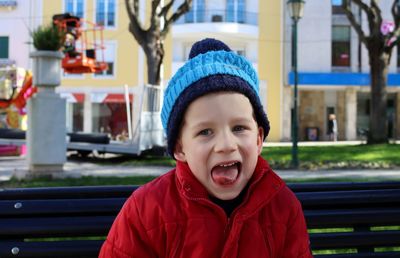 Portrait of a  boy in a red jacket and blue hat. a joyful boy makes faces and sticks out his tongue.