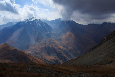 Alpine gorge with snow-capped peaks in sunlight in autumn, sky with clouds