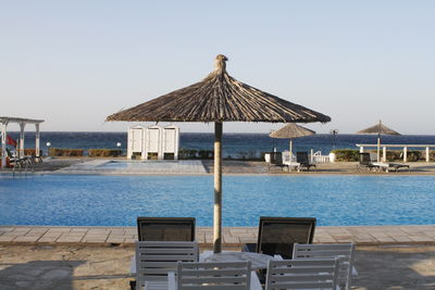 Lounge chairs by swimming pool at beach against clear sky