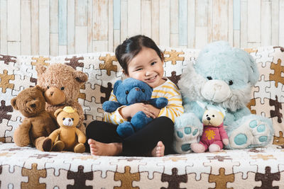 Portrait of girl sitting with teddy bears on sofa at home