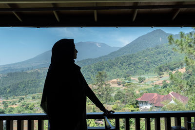 Man standing by railing on mountain against sky